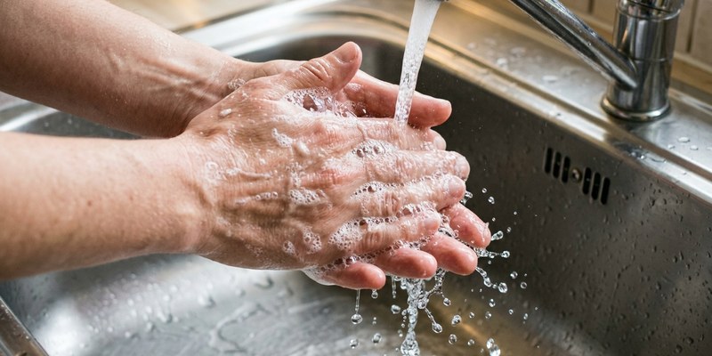 Manos enjabonándose bajo el agua corriente en un fregadero de acero inoxidable